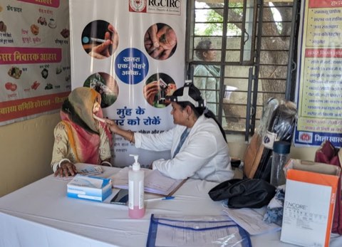 An oral cancer screening session run with the Rajiv Gandhi Cancer Institute, with tobacco-risk material displayed behind.