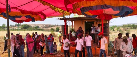 A community health awareness gathering under a shamiana, with villagers watching a street play by the team.