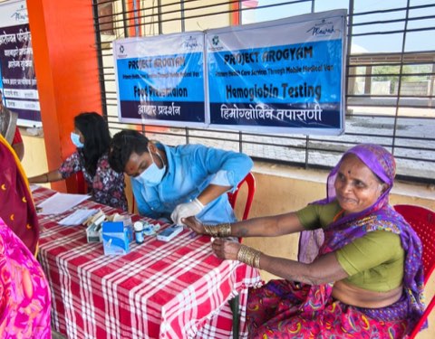 Haemoglobin testing alongside a food demonstration counter at a village camp.