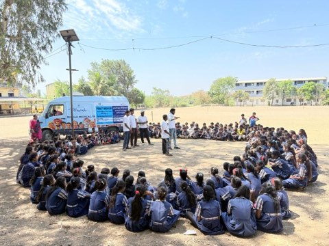 A school health session: students seated in a circle around the team, with the mobile medical van behind them.