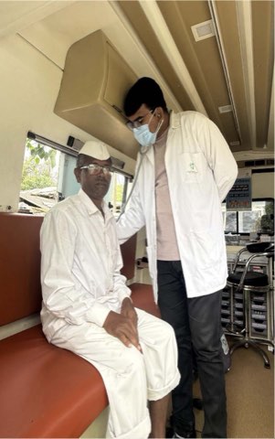A doctor examining a seated patient with a stethoscope inside the mobile medical van.