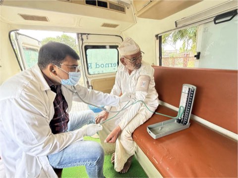 Blood pressure being taken from an elderly man on the bench inside the van, with a mercury sphygmomanometer beside him.