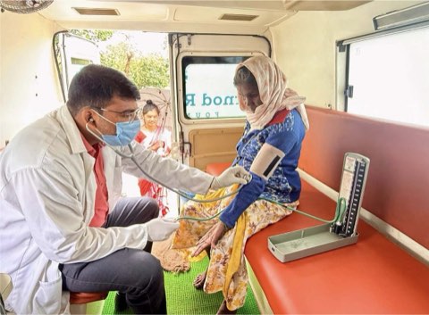 Blood pressure being taken from an elderly woman inside the van, while the next patient waits at the open door.