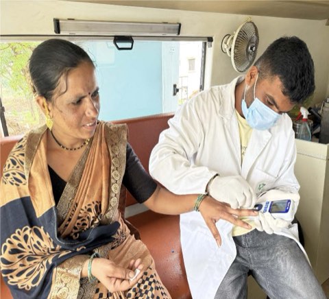 A point-of-care blood test being taken from a woman's finger inside the mobile medical van.