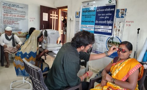 An eye check-up camp at Kaudasar: a trial frame being fitted for refraction, with an autorefractor in use behind.